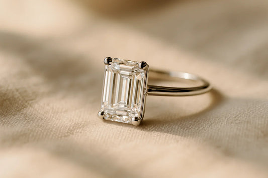 Elongated emerald cut diamond solitaire engagement ring in white gold, showing the step-cut facets across the open table