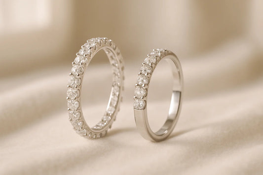 A full diamond eternity band with stones all the way around beside a half eternity band with diamonds across the front, both in white gold on ivory velvet.