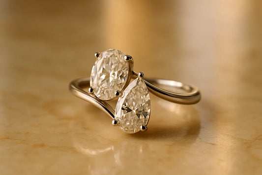 Toi et moi engagement ring with two diamonds, an oval beside a pear, in a white-gold bypass setting resting on warm marble.